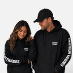 A man and a woman wearing matching black hoodies with white 'TANTRUM TRADES' text on the chest and sleeves, posed against a clean light gray background.