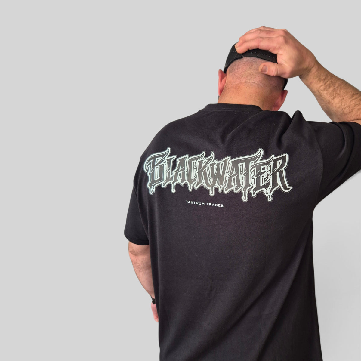 A man shown from behind wearing a black t-shirt with a large white and black 'Blackwater' graphic on the back, underneath sits 'Tantrum Trades' set against a solid gray background.