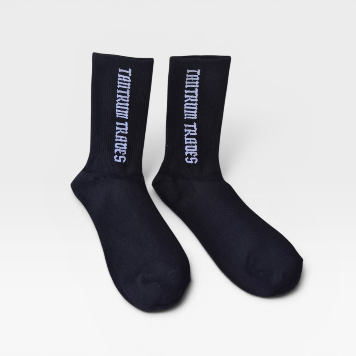 A pair of black crew socks with white vertical text reading 'TANTRUM TRADES' on the sides, displayed against a light gray background.