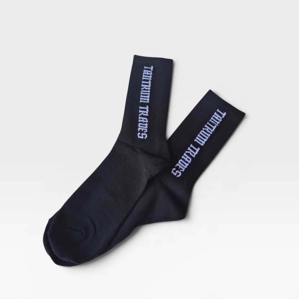 A pair of black crew socks with white logo text reading 'TANTRUM TRADES' printed vertically on the cuffs, displayed on a clean light gray background.